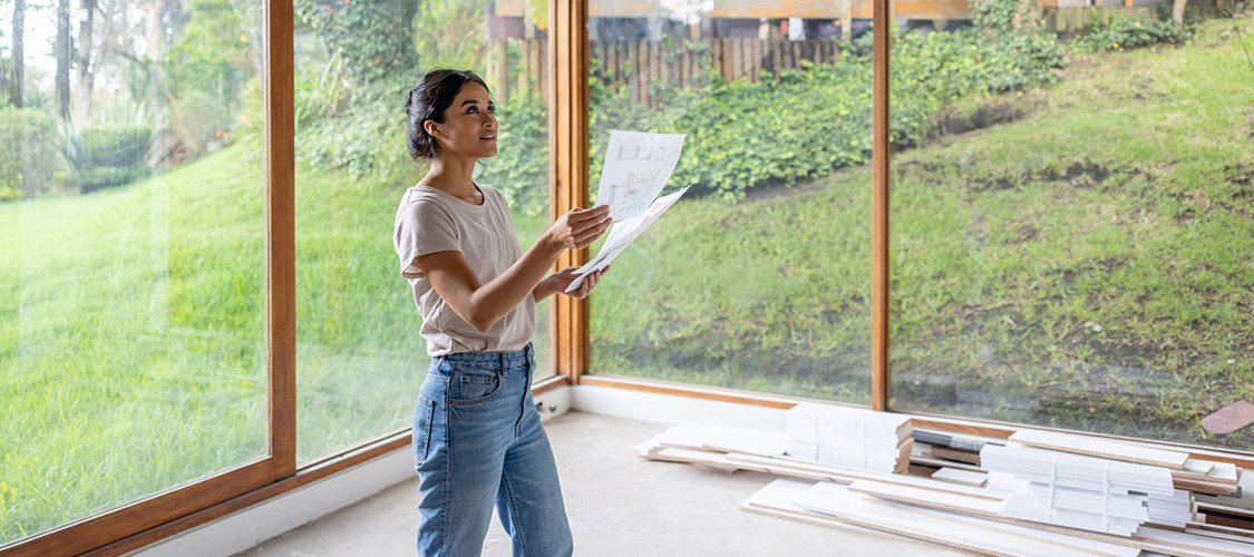  A woman in an empty room going over renovation plans.