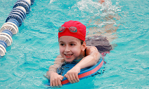 Deklica, ki obiskuje plavalni tečaj za otroke, v bazenu čofota z učnim pripomočkom