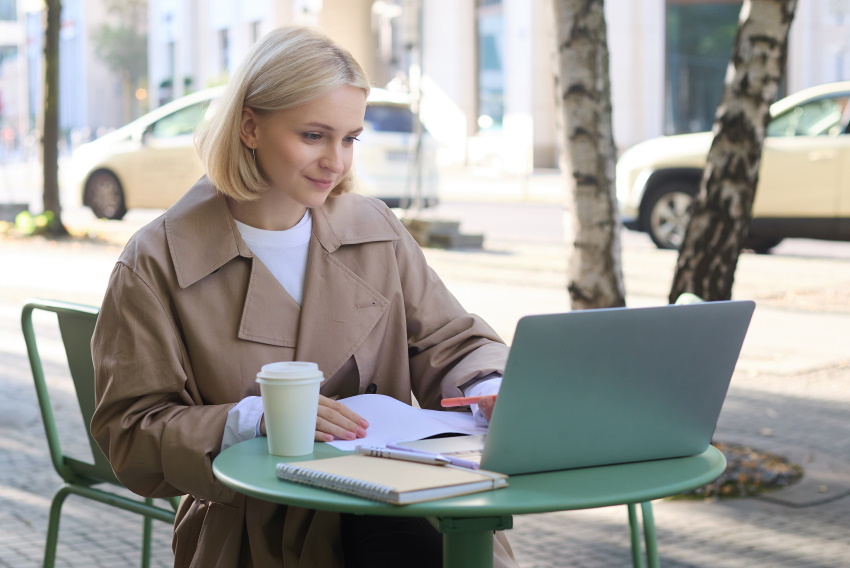 Ženska sedi v kavarni in samozavestno pregleduje svoj mesečni proračun, saj ve, kaj je varčevanje in za kaj varčuje.