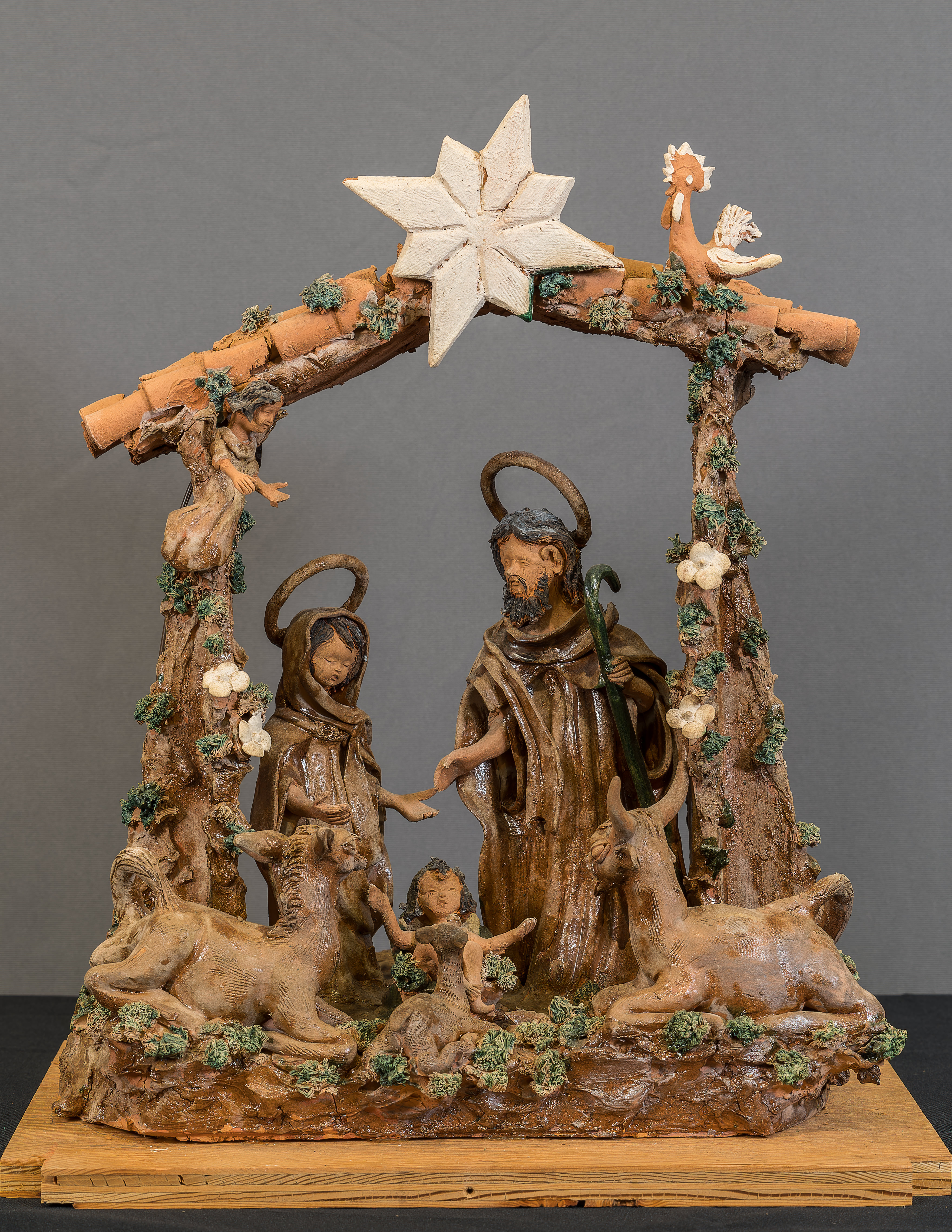 Photo of a clay Nativity scene from Portugal featuring the Holy Family within a stable. An ox, donkey, and rooster look upon them. 