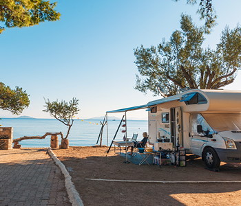 Avtodom z razprto tendo, parkiran na obali ob sončnem zahodu.