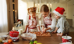 Mama z dvema majhnima otrokoma v rustikalni kuhinji ustvarja božične dobrote