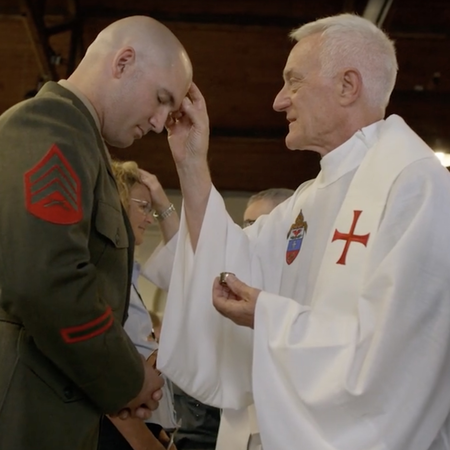 A Catholic Priest in miltary robe blesses a military veteran with Holy Water