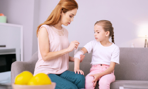 Mama hčerki v apartmaju nudi prvo pomoč po tem, ko si je odrgnila komolec.