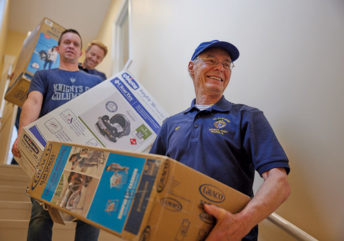 Tom Jenn (right) and fellow members of St. Clement Council 12407 in Dunlap, Ill., carry a load of car seats and other baby equipment to the Women&rsquo;s Care Center&rsquo;s supply room in December.