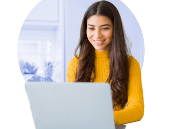 Smiling young woman in a yellow sweater working on a laptop at home.