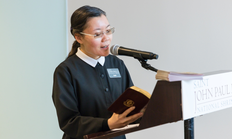 A female Shrine staff member reading from the Diary of Saint Faustina at a podium