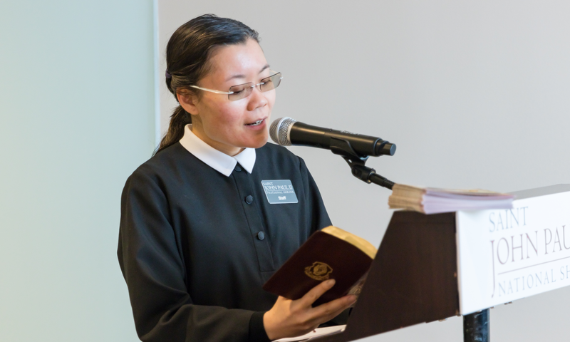 A female Shrine staff member reading from the Diary of Saint Faustina at a podium