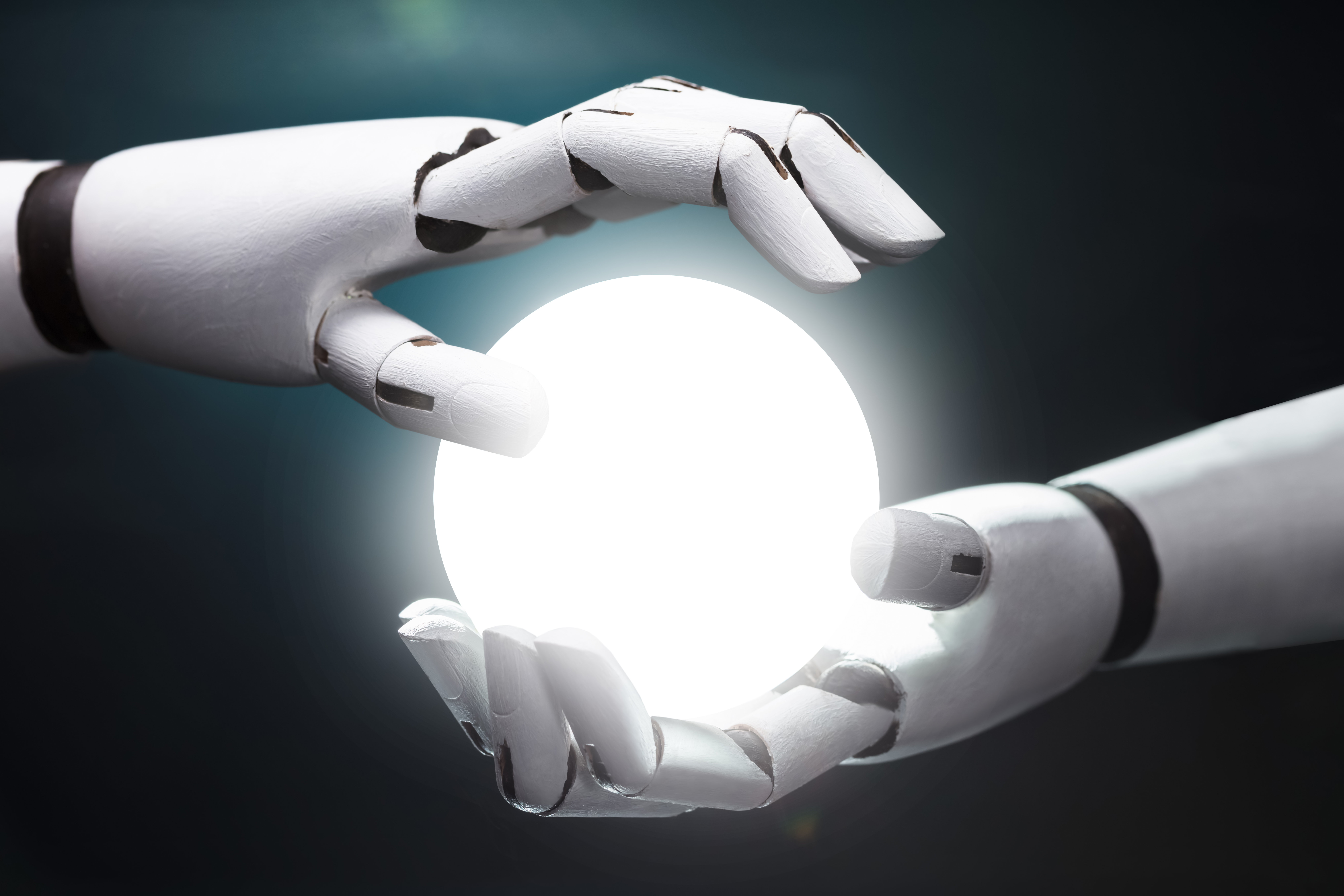 A close-up of two white, articulated robotic hands positioned as if they are carefully holding or hovering around a brilliant, glowing white orb of light. The background is a dark, moody blue, emphasizing the radiance of the sphere and the sleek texture of the robotic fingers.