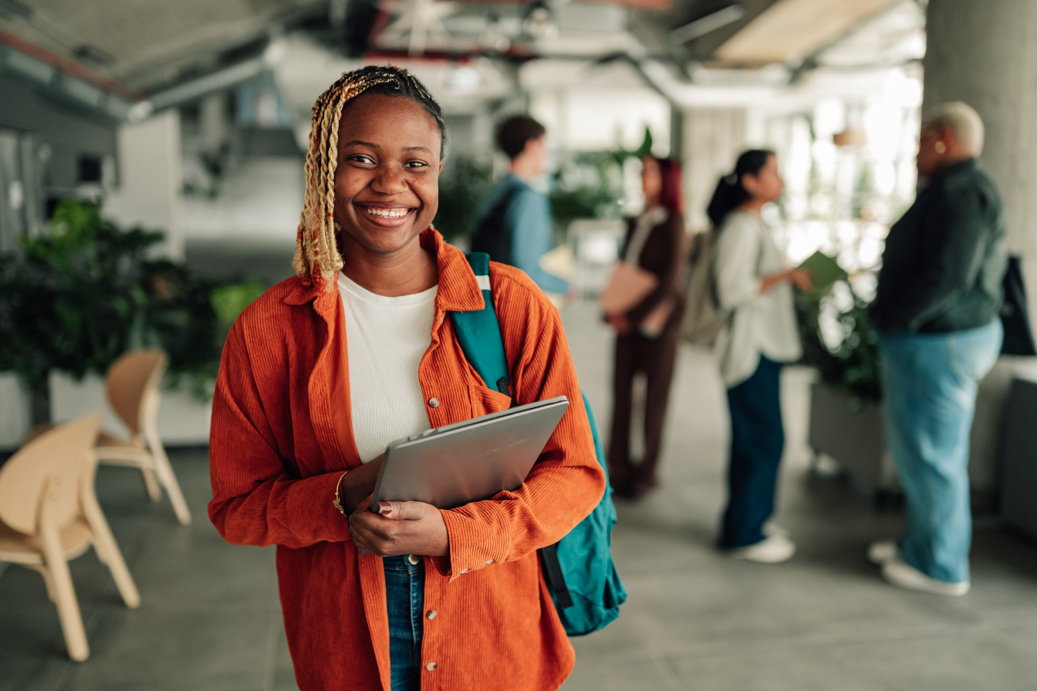Smiling young black woman holding a laptop, standing in an office space 