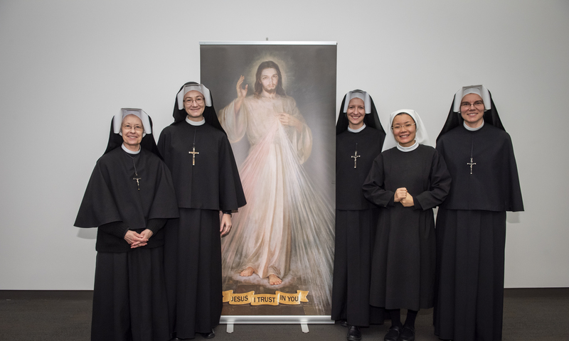 Five nuns standing next to a painting of Jesus at the John Paul II Shrine.