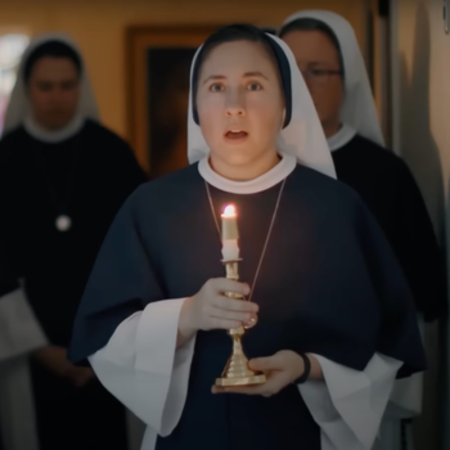 Group of nuns in prayer with holding candles in a peaceful chapel setting.