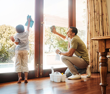 Oče in otrok pomivata okna med spomladanskim čiščenjem - oče otroka uči pomoči pri domačih opravilih