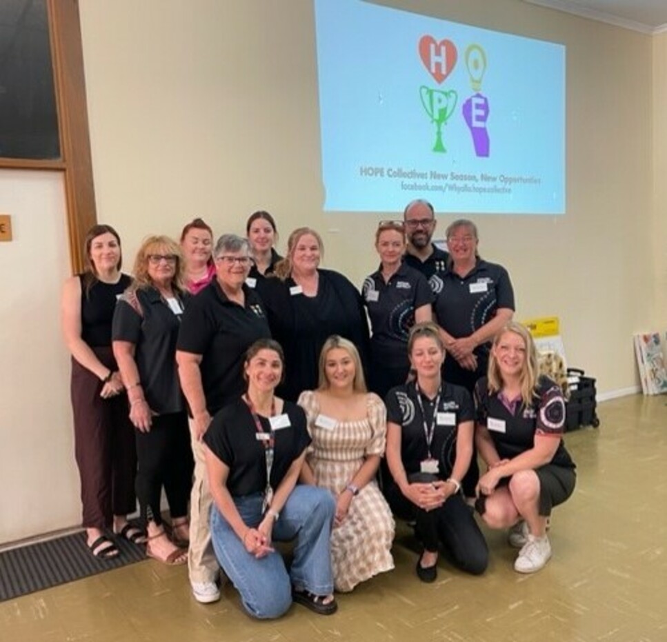 Group photo of Whyalla HOPE Collective team members at a community event with presentation slide behind reading ‘New Season, New Opportunities’