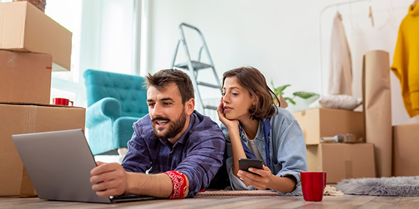 a couple lays on the floor in their living room looking at a tablet together and talking 