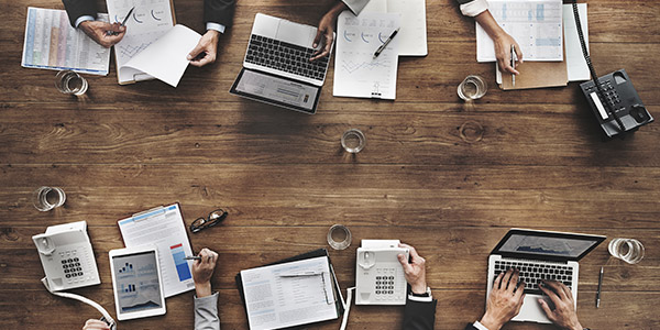 An overhead view of different work tools like laptops, a tablet, and papers sitting on a desk