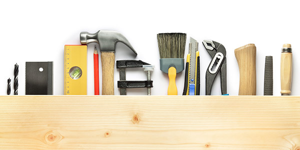 Home tools lined up next to each other including a paint brush, a hammer, a screwdriver etc. 