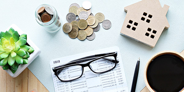Various objects sit on top of a desk including glasses, coins, a model of a house, and coffee