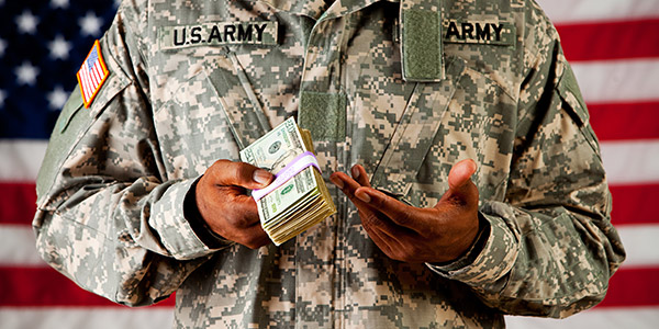 A Black man in a American military uniform holds a stack of 50 dollar bills