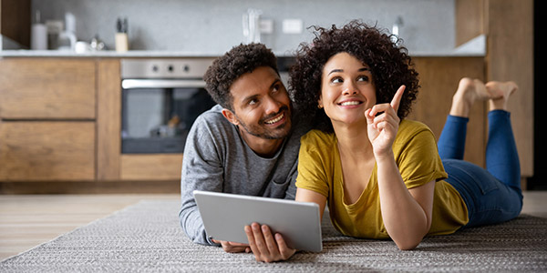 A Black woman and man sit smiling in their home as they plan their future