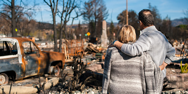 A man and woman stand with their arms around each other looking at the remains of their home