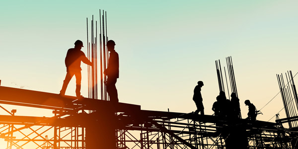 Silhouettes of construction workers standing on the beams of a building under construction