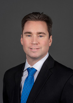 Headshot of Tim Kirwan, who smiles while wearing a black suit and a blue tie