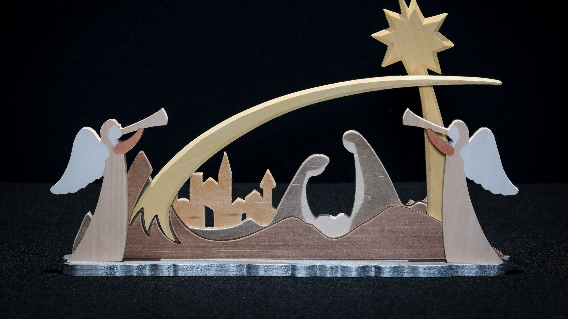 Carved wood nativity scene that includes the Holy Family beneath a star with a city silhouette in the background. Two angels complete the scene.