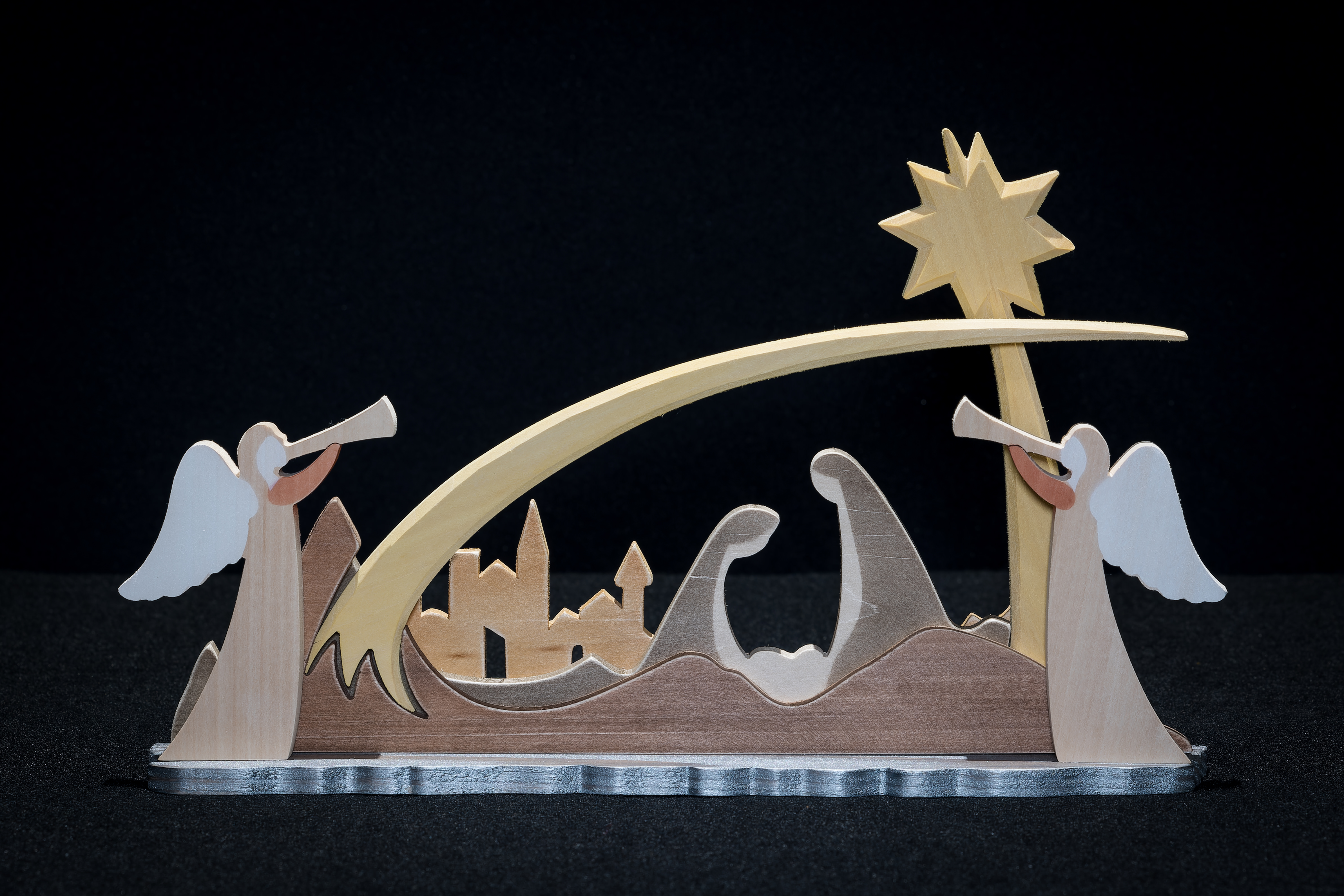 Carved wood nativity scene that includes the Holy Family beneath a star with a city silhouette in the background. Two angels complete the scene.