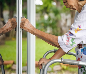 Starejša gospa s hojico odklepa vrata v svoj dom, ki je varnostno prilagojen za starejše.