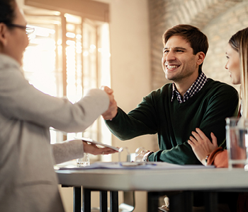 Zadovoljen mlad par se rokuje z zavarovalnim zastopnikom. Simbolna fotografija za članek o vinkulaciji.