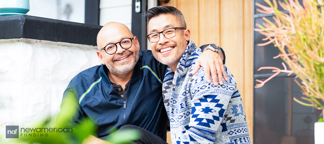 Two men sit smiling on their porch with their arms around each other