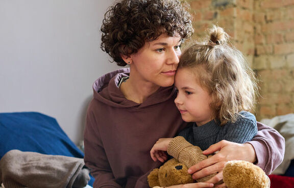 Woman hugging child holding teddy bear