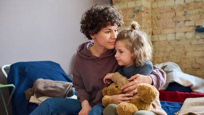 Woman hugging child holding teddy bear