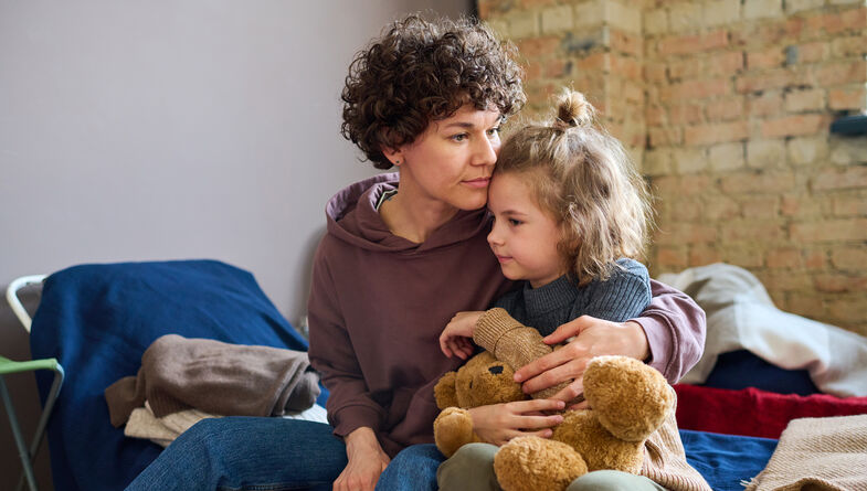 Woman hugging child holding teddy bear