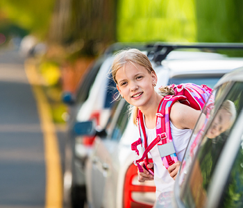 Deklica prečka cesto med parkiranimi avtomobili