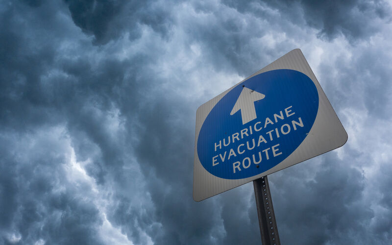 Composite image of a hurricane evacuation route sign against a stormy sky.